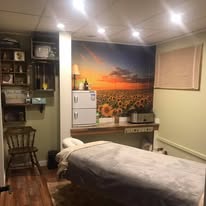 Treatment room with sunset-over-sunflower-field wall mural, massage table, hardwood floors